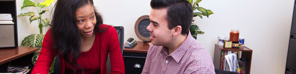 An advisor talking with a student at a desk.